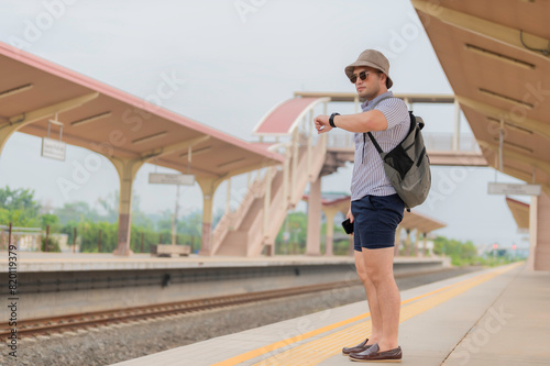 Handsome young man with a backpack uses the phone while standing near the railroad train on the platform,Tourism and travel in the summer. Vacations for the student.