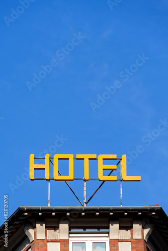 Enseigne avec le mot 'HOTEL' écrit en lettres capitales jaunes lumineuses sur le toit d'un immeuble sur fond de ciel bleu. Espace négatif photo