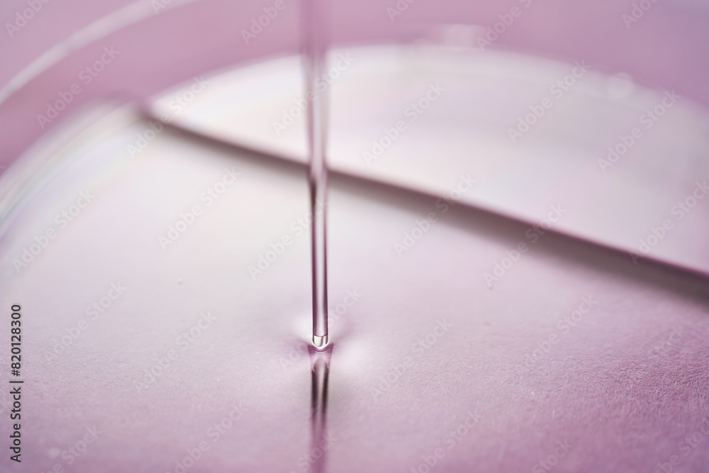 Serum or cosmetic oil flows into a transparent bowl on a purple background.
