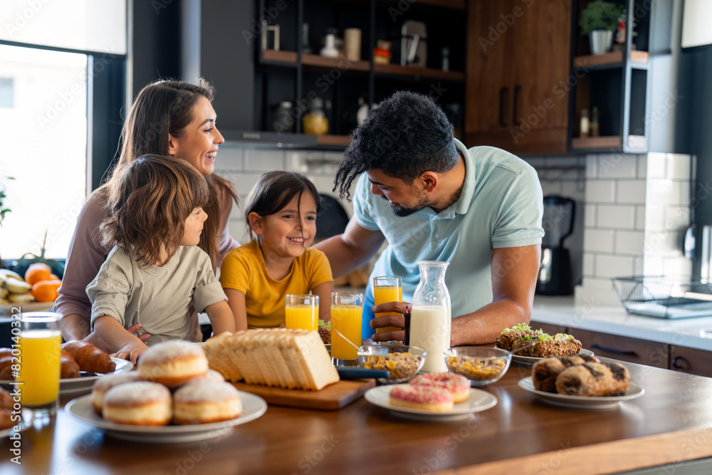Small lovely boy and girl having rich delicious breakfast in the morning with mother and father in the kitchen at home. Small lovely boy and girl having rich delicious breakfast in the morning with mother and father in the kitchen at home.