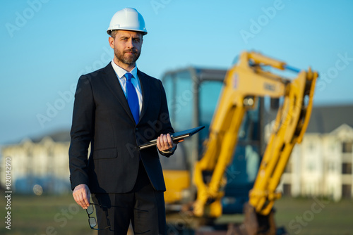 Builder engineer or civil engineer worker at a construction site. Engineer worker in suit and helmet at construction site. Supervisor construction manager near excavator. Renovation building concept.