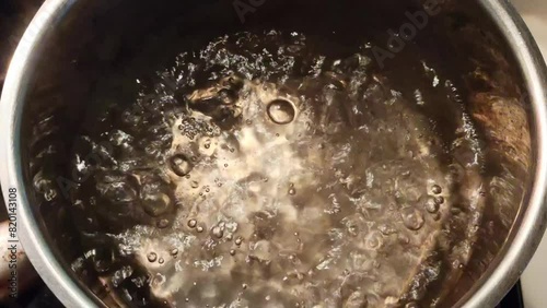 Boiling water with steam rising and bubbles forming in a stainless steel pot