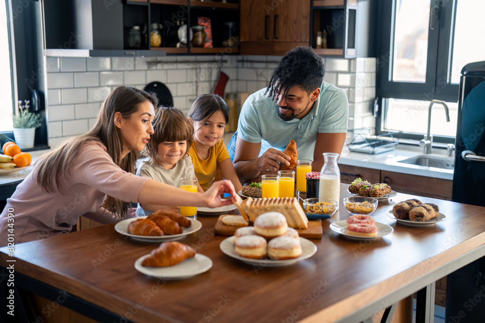 Small cute boy and girl eating breakfast with mother and father in the kitchen at home. Small cute boy and girl eating breakfast with mother and father in the kitchen at home.