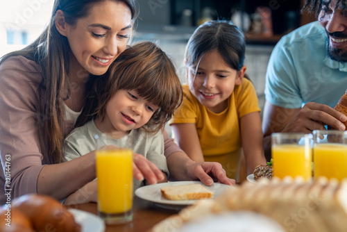 Smiling young mother preparing breakfast for her children while sitting at the table with them and her husband.