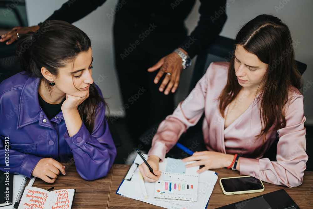 Fototapeta premium In the office environment, two professional women engage in a focused, strategic discussion over business analytics, demonstrating effective teamwork and collaboration.