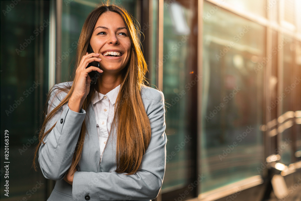 A beautiful Caucasian woman, the CEO of a company, is talking on the phone while standing in front of an office building. A beautiful Caucasian woman, the CEO of a company, is talking on the phone while standing in front of an office building.