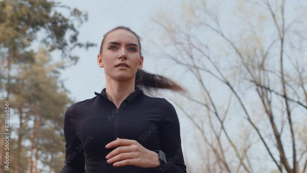 Young caucasian female jogger in a black sportswear running with a confident face on an alley in an autumn city park close up, bottom view. Concept of modern outdoor sports training in a casual urban