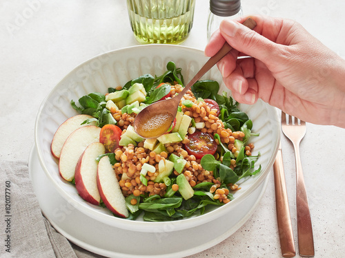 Close-up view: hand holding spoon with vinaigrette dressing salad of greens, lentils, avocado and apple. Healthy food.