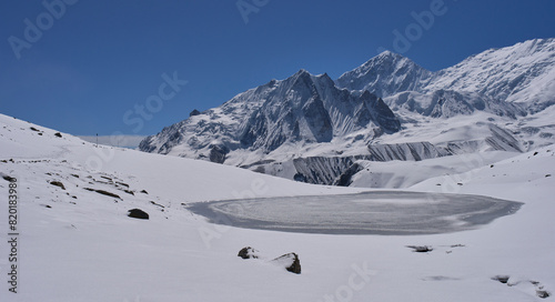 A hiking trail to the Tilicho Lake, Annapurna Conservation area, Nepal. A small lake covered in ice. A trail covered in snow and ice. Frozen lake. Mountain range. photo