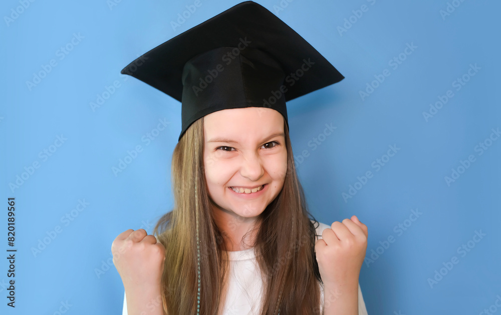 Sweet, smart, cheerful, cheerful, confident student-scientist girl with graduation hat on her head. Isolated on blue background. Rejoices at victory. Sweet, smart, cheerful, cheerful, confident student-scientist girl with graduation hat on her head. Isolated on blue background. Rejoices at victory.