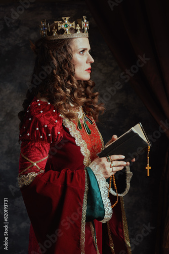 medieval queen in red dress with book, rosary and crown