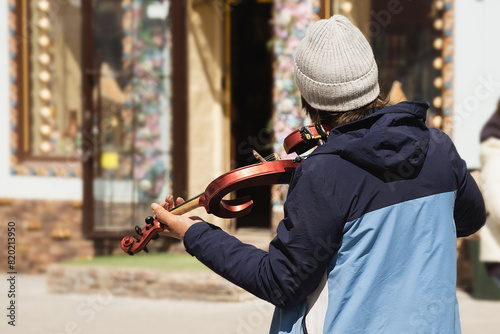 A man on the street is playing the violin, view from the back