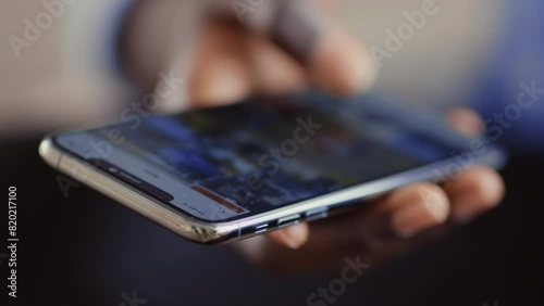 Online life. African guy scrolling social media app on cellphone, close up photo