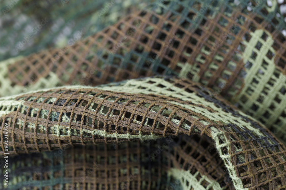 Obraz premium A piece of camouflage fabric with a green and brown pattern. The fabric is made of a mesh material and has a rough texture