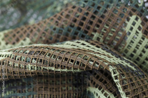 A piece of camouflage fabric with a green and brown pattern. The fabric is made of a mesh material and has a rough texture