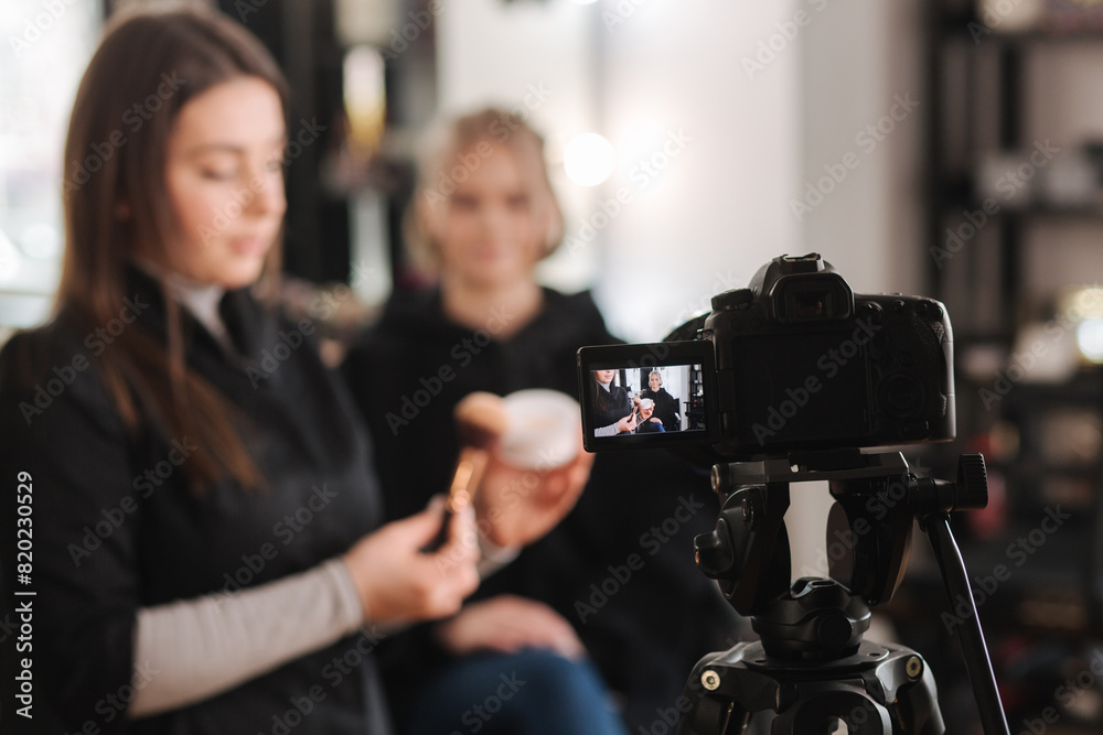 Woman making a video for her blog of making makeup, digital camera on tripod. Young female blogger on camera screen holding cosmetics
