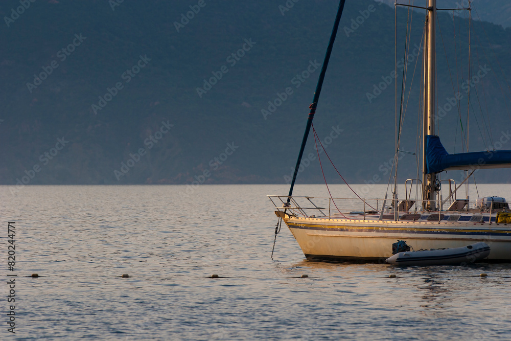 Sailing boat on bleu sunset background. Sailing boat on the sea. A sailboat at anchor in the Gulf of Porto in Corsica. Sailing boat on bleu sunset background. Sailing boat on the sea. A sailboat at anchor in the Gulf of Porto in Corsica.