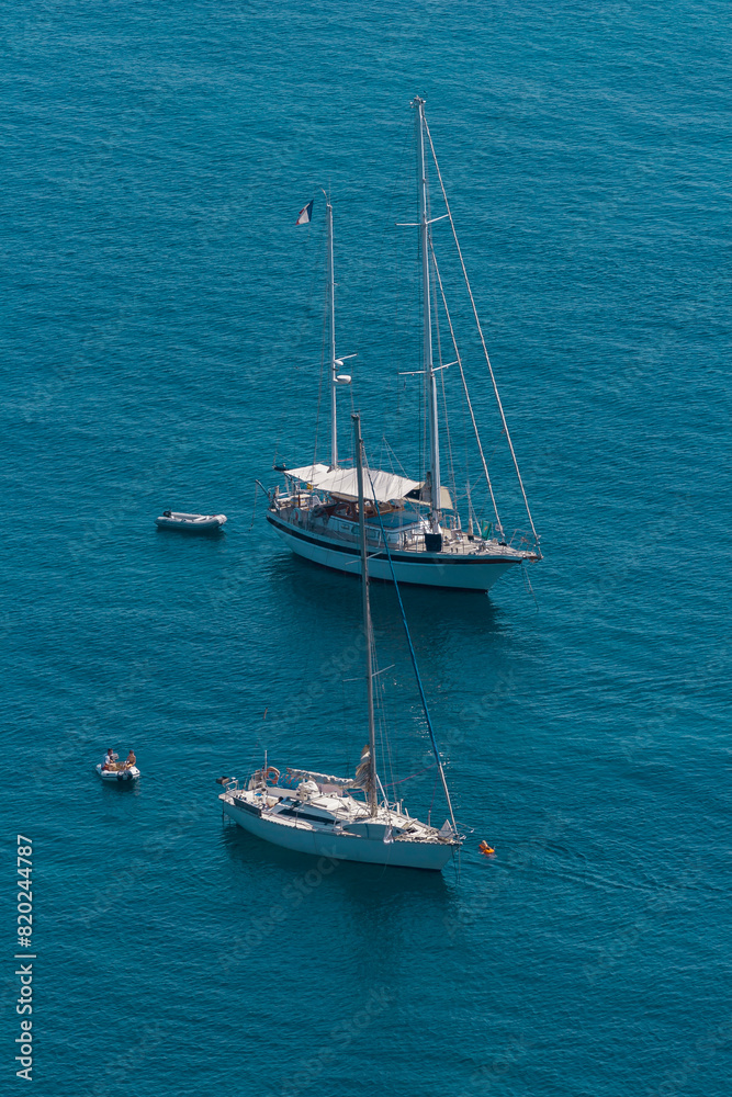 Sailboats at anchor in Corsica. Sailboats floating on the calm blue sea. Coastal summer landscape of Corsica Sailboats at anchor in Corsica. Sailboats floating on the calm blue sea. Coastal summer landscape of Corsica