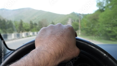 Wallpaper Mural A person drives a car with one hand on the steering wheel, navigating a scenic mountain road with lush green trees. Torontodigital.ca