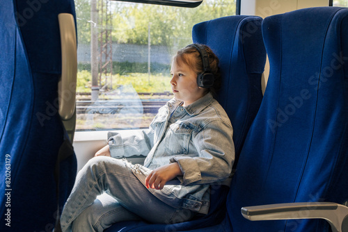 Relax on the train. The girl is traveling on a long-distance and short-distance train with a thoughtful face, listening to music in headphones. Selected focus.