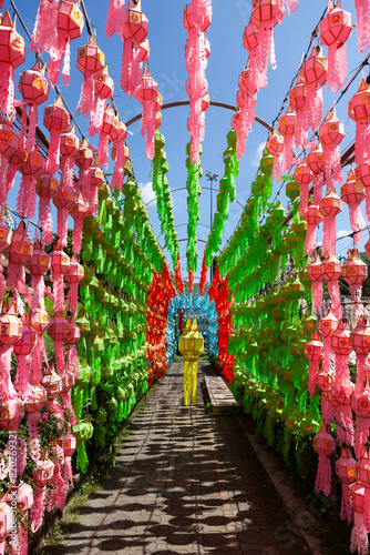 Colourful lanterns in Lamphun town near Chiang Mai during Loy Krathong festival. Green, Red and Pink lanterns tunnel under blue sky.