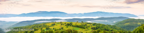 panorama of ukrainian mountainous rural landscape at sunrise. trees and agricultural fields on hills rolling in to the distant valley full of fog. ridge beneath a sky with clouds in morning light photo