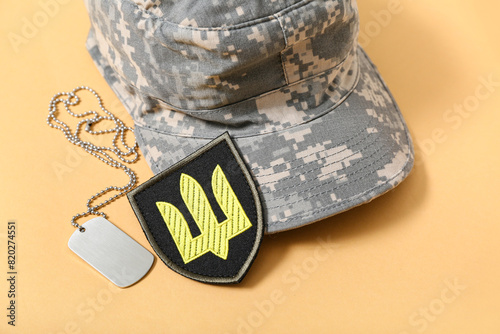Badge of Ukrainian army with trident, military tag and hat on beige background