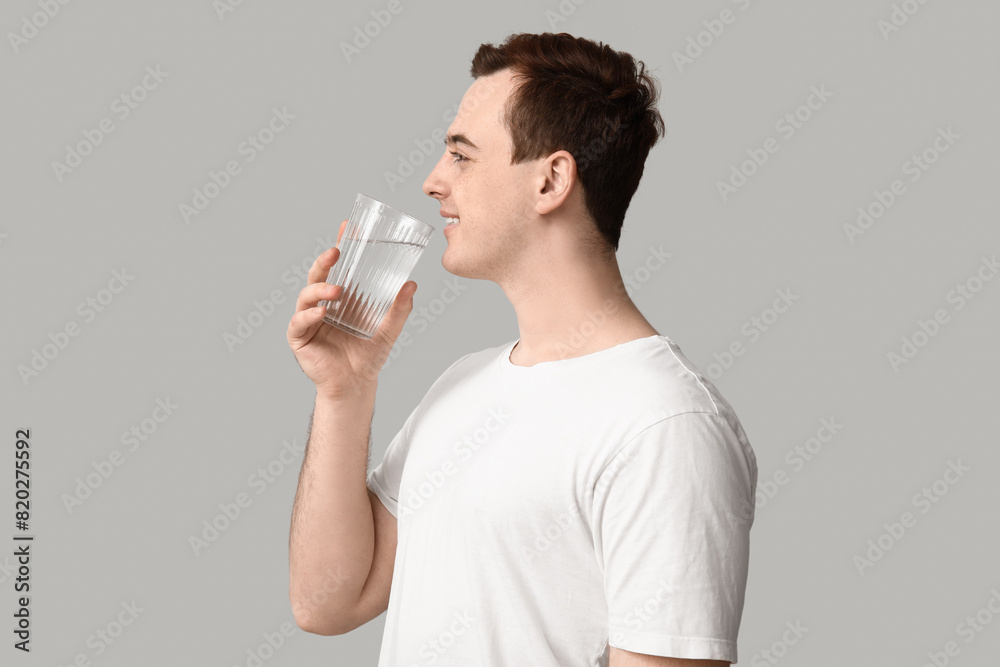 Handsome young man drinking clean water on grey background Handsome young man drinking clean water on grey background