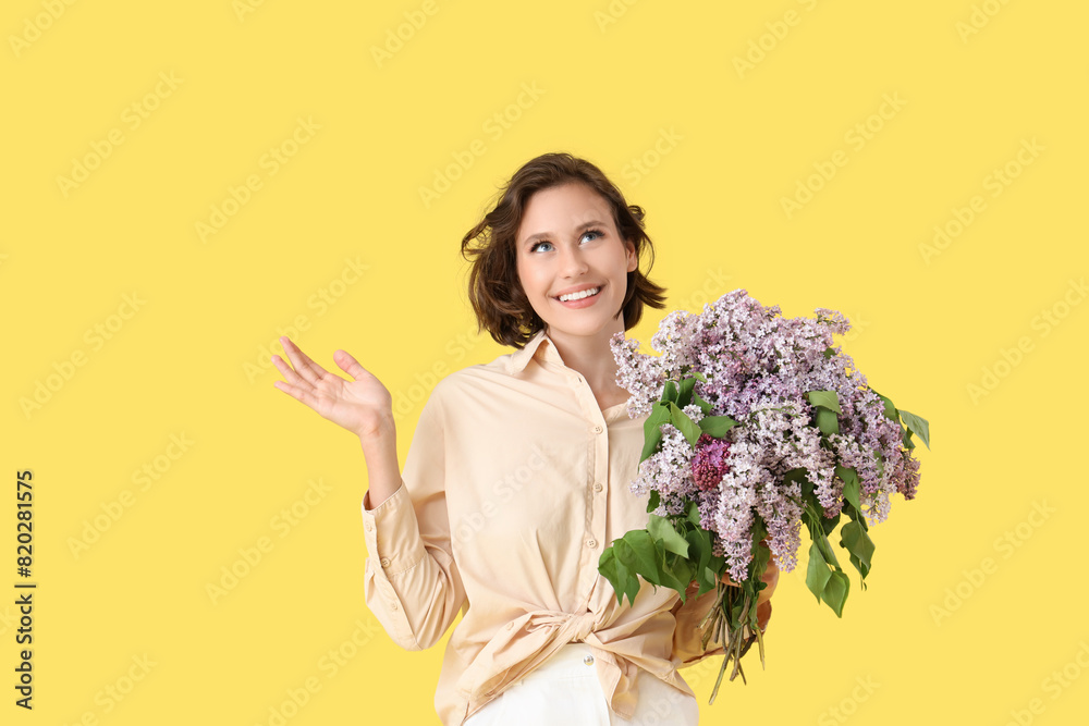 Happy young woman with bouquet of blooming lilac flowers on yellow background