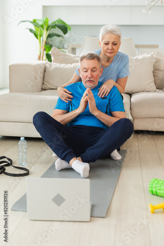 Yoga mindfulness meditation. Senior adult mature couple practicing yoga with online lessons in laptop. Old wife helping teaching husband meditating relaxing. Family doing breathing practice at home