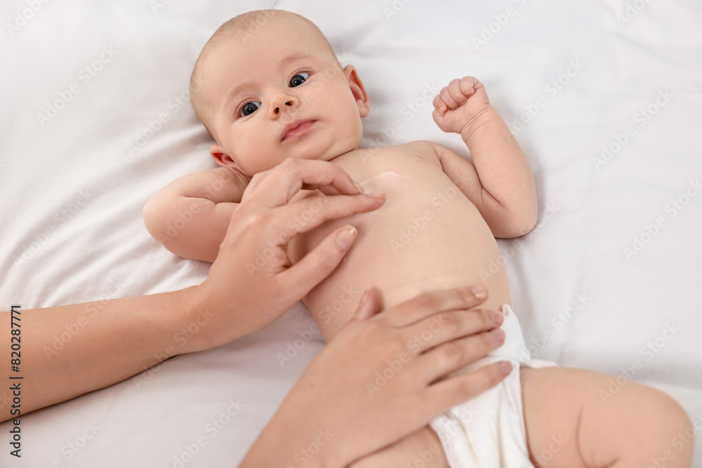 Woman applying body cream onto baby`s skin on bed, closeup Woman applying body cream onto baby`s skin on bed, closeup