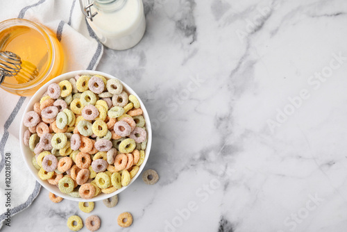 Tasty cereal rings in bowl, milk and honey on white marble table, flat lay. Space for text