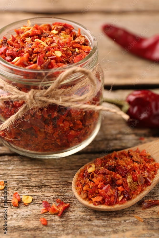 Chili pepper flakes in jar and spoon on wooden table, closeup Chili pepper flakes in jar and spoon on wooden table, closeup