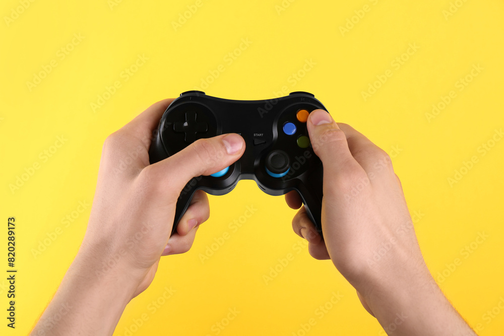 Man using wireless game controller on yellow background, closeup Man using wireless game controller on yellow background, closeup
