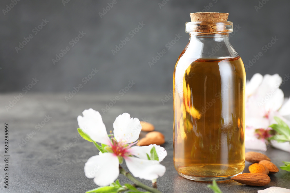 Almond oil in bottle, flowers and nuts on grey textured table, closeup. Space for text Almond oil in bottle, flowers and nuts on grey textured table, closeup. Space for text