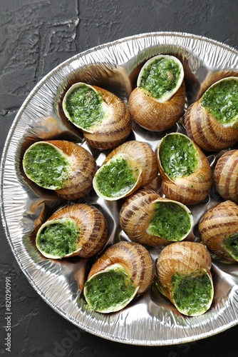 Delicious cooked snails on dark textured table, top view