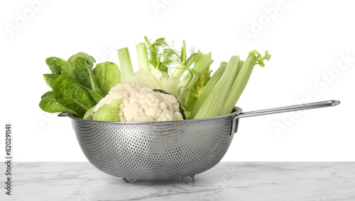 Metal colander with different vegetables on marble table against white background