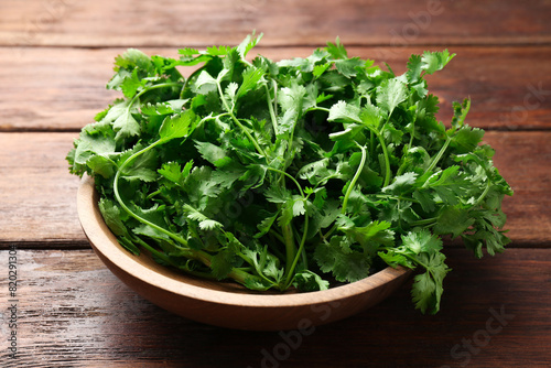 Fresh coriander in bowl on wooden table, closeup