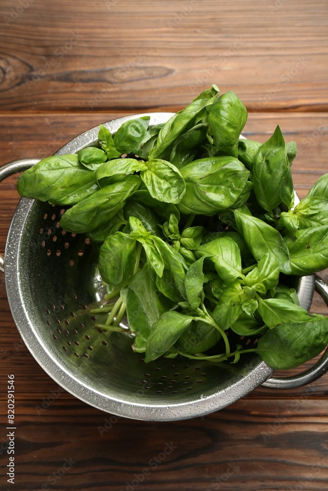 Metal colander with fresh basil leaves on wooden table, top view Metal colander with fresh basil leaves on wooden table, top view