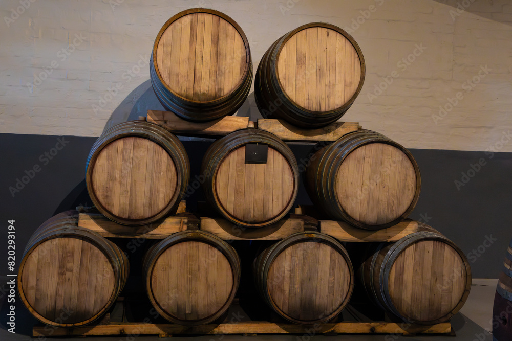 Wooden oak wine barrels in a cellar stacked on top of each other in an triangle formation. 