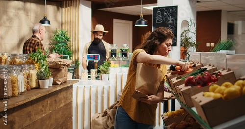 Tracking shot of woman in zero waste supermarket using nonpolluting paper bag while shopping for vegetables. Client in local shop using no single use plastics policy to save planet photo