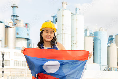 Portrait of teenage girl in blue overalls with flag of Laos in her hands against the backdrop of a modern metallurgical plant photo