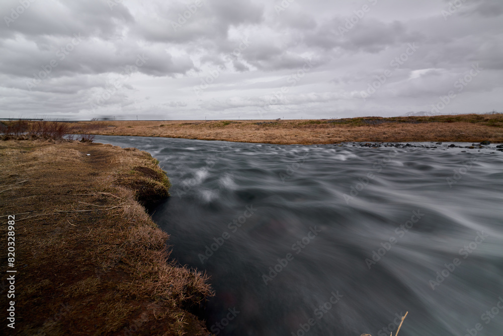 Long exposure photo of Icelandic river with brown meadow background and cloudy day