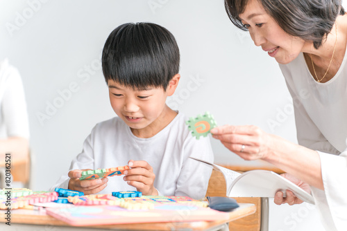 学校の教室でアルファベットのおもちゃを使って英語を勉強する小学生低学年の男の子と女性教師
 photo