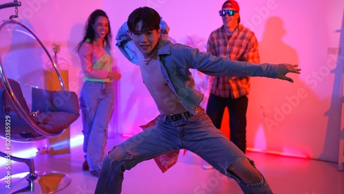 Attractive asian dancer with casual cloth dancing and looking at friend cheering him. Caucasian man and hispanic hipster perform street dancing while turn around and looking at happy team. Regalement. photo