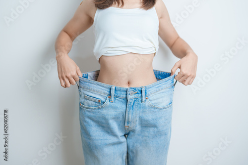 young slim female wearing big or oversize jeans, woman show healthy shape after weight loss. dieting, exercise, body fit and liposuction surgery concept