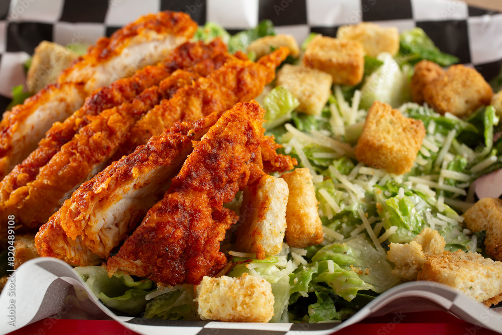 A closeup view of a Caesar salad, with Nashville chicken strips.