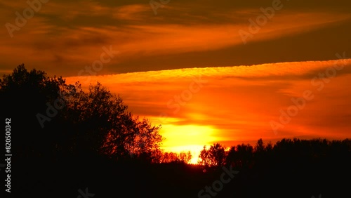 Deep orange sunset sky with plane chemtrail and forest silhouette, Latvia