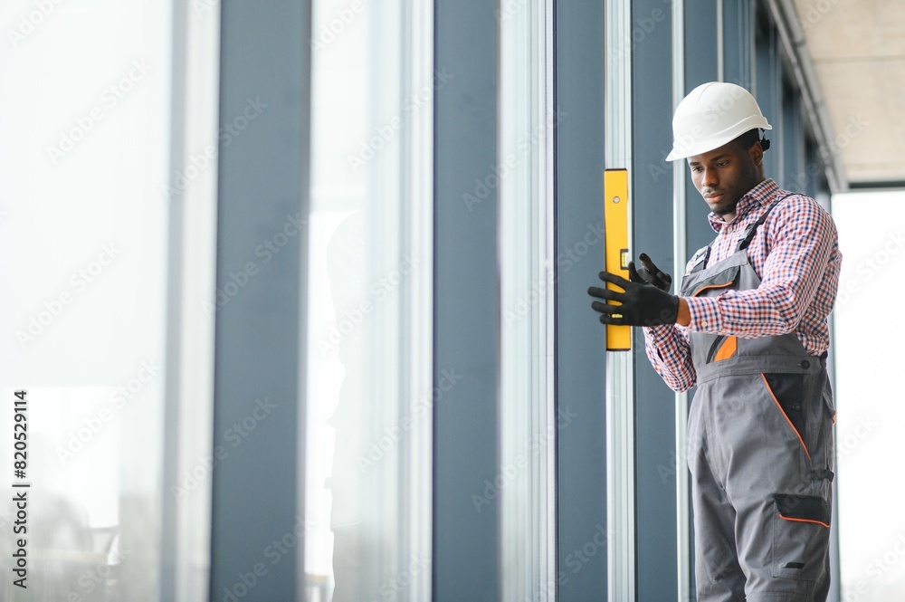 Low Angle View Of A Young African Repairman In Overalls Installing Window Low Angle View Of A Young African Repairman In Overalls Installing Window