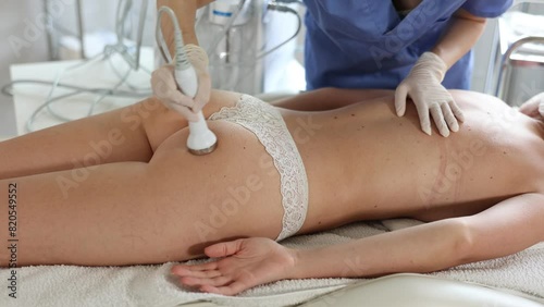 Aesthetician administering hardware procedure on buttocks of young female patient in cosmetology clinic, using high frequency ultrasound head to open skin pores for deep penetration of nutrients
